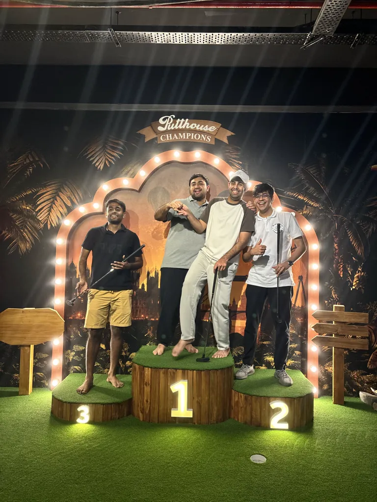 Four friends celebrating on the Putthouse Champions podium with their putters