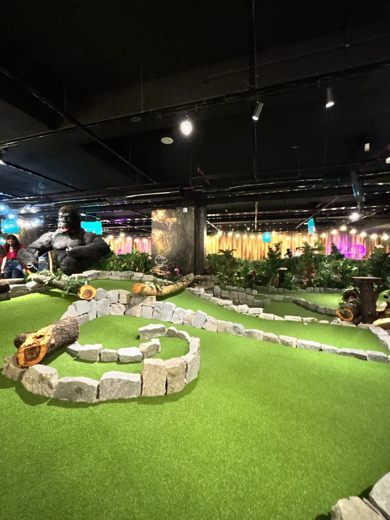 A winding stone-edged hole on the jungle-themed mini golf course at Putt House, with a life-size gorilla behind it